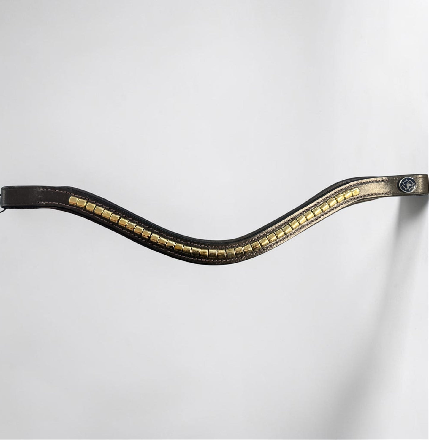 A browband with a wavy, S-shaped curve, featuring a row of gold-toned rectangular studs or metallic accents along the center and a small circular blue emblem near the bottom.