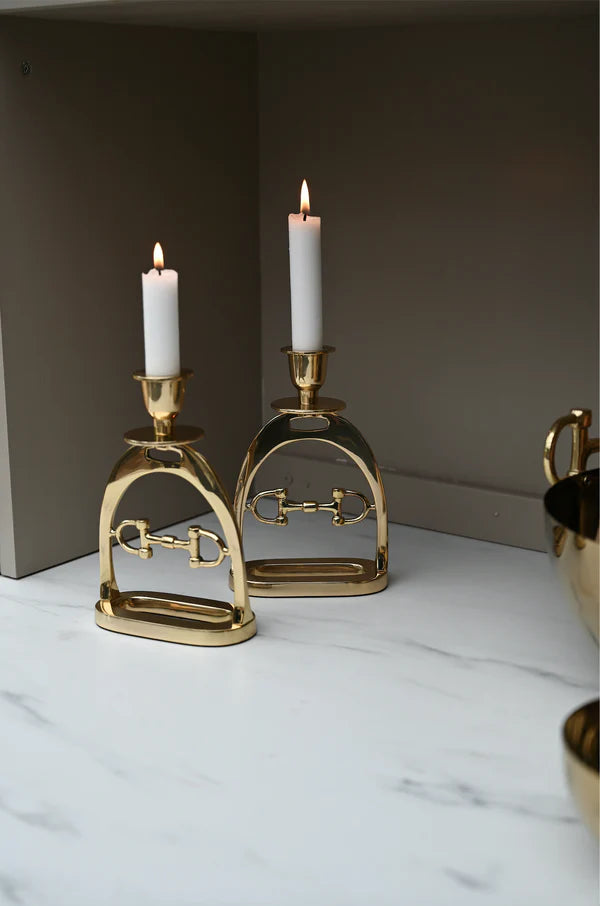 Gold equestrian-themed candle holders with candles on a marble surface.