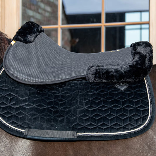 Black quilted saddle pad with black flocked sides on a horse, blurred indoor background