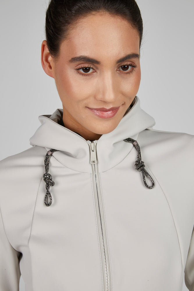 Woman wearing a light gray hoodie with a zipper and drawstrings on a plain background