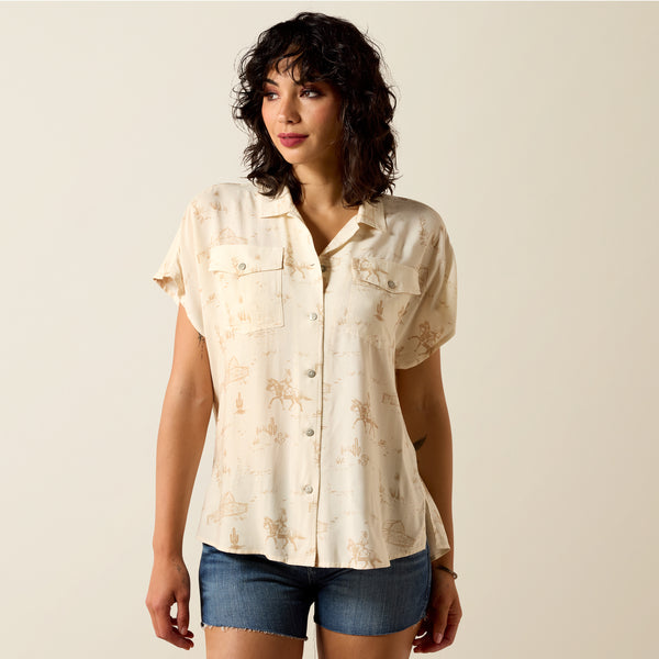 Woman wearing a beige floral short-sleeve shirt and denim shorts against a beige background