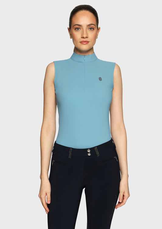 Woman wearing a blue sleeveless top and black breeches on a beige background