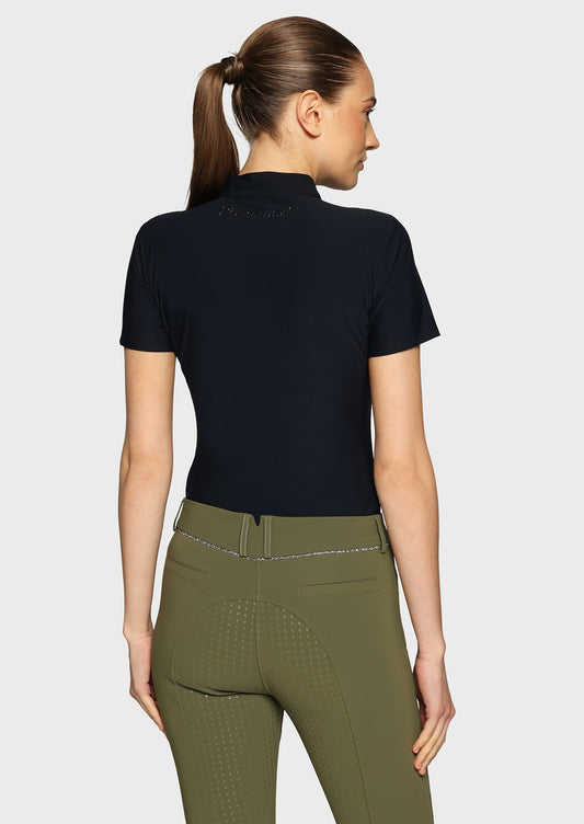 Woman wearing a navy top and olive breeches on a beige background