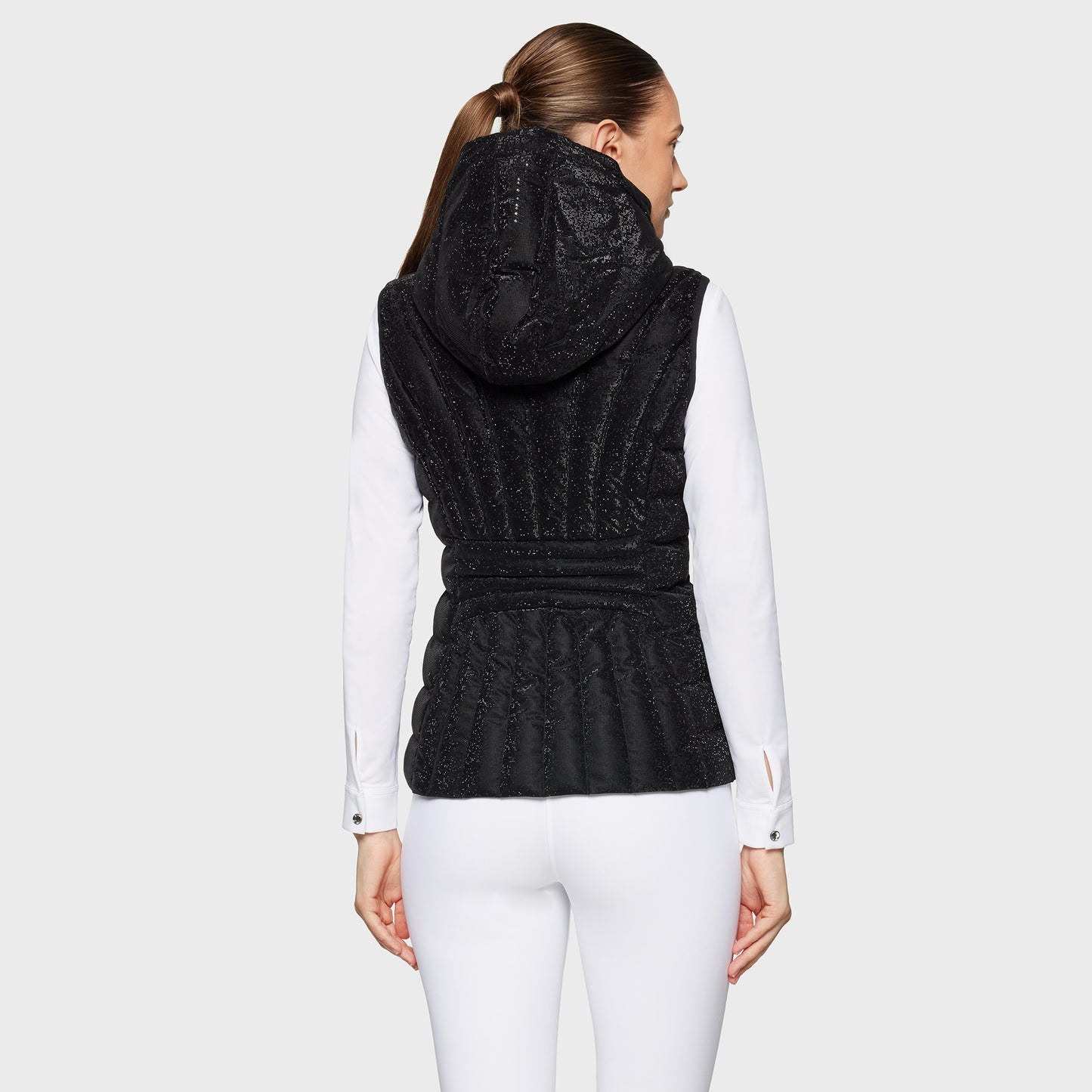 Woman wearing a black vest over a white long-sleeve shirt on a light gray background