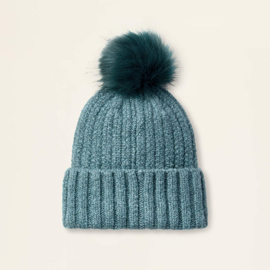 Teal knit beanie with a fur pom-pom on a light beige background