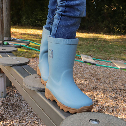 Child wearing blue rubber boots with brown soles on a playground.
