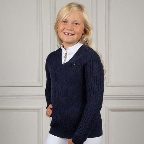 Young girl wearing a navy sweater over a white shirt against a light gray wall.