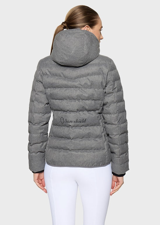 A woman shown from the back wearing a heather gray puffer jacket with horizontal quilting, a hood, and a small black script logo on the back, paired with white leggings against a light gray studio background.