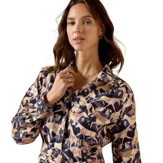 A woman wearing a long-sleeve button-up dress with a beige, brown, and navy blue abstract camouflage pattern, photographed against a solid white background.