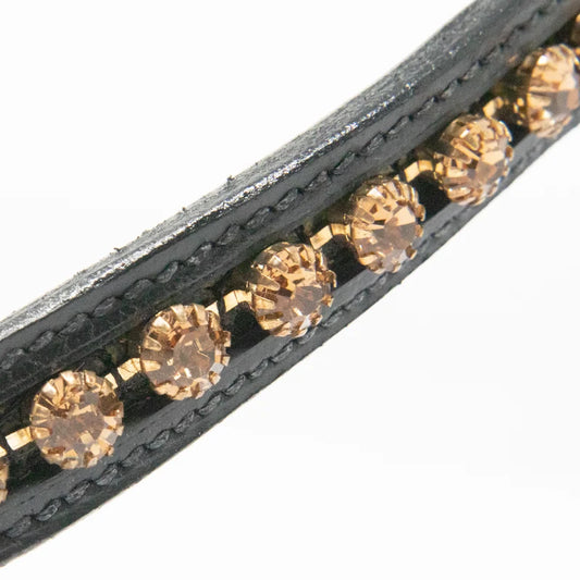 Close-up of a black leather browband featuring a row of faceted champagne-colored rhinestones set in gold-toned metal, against a plain white background.