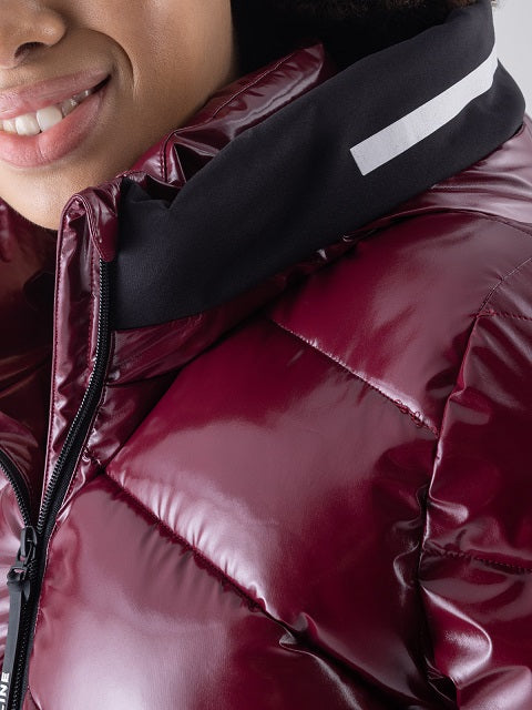 Woman wearing a glossy burgundy puffer jacket with a black collar featuring a reflective white stripe, worn by a model.