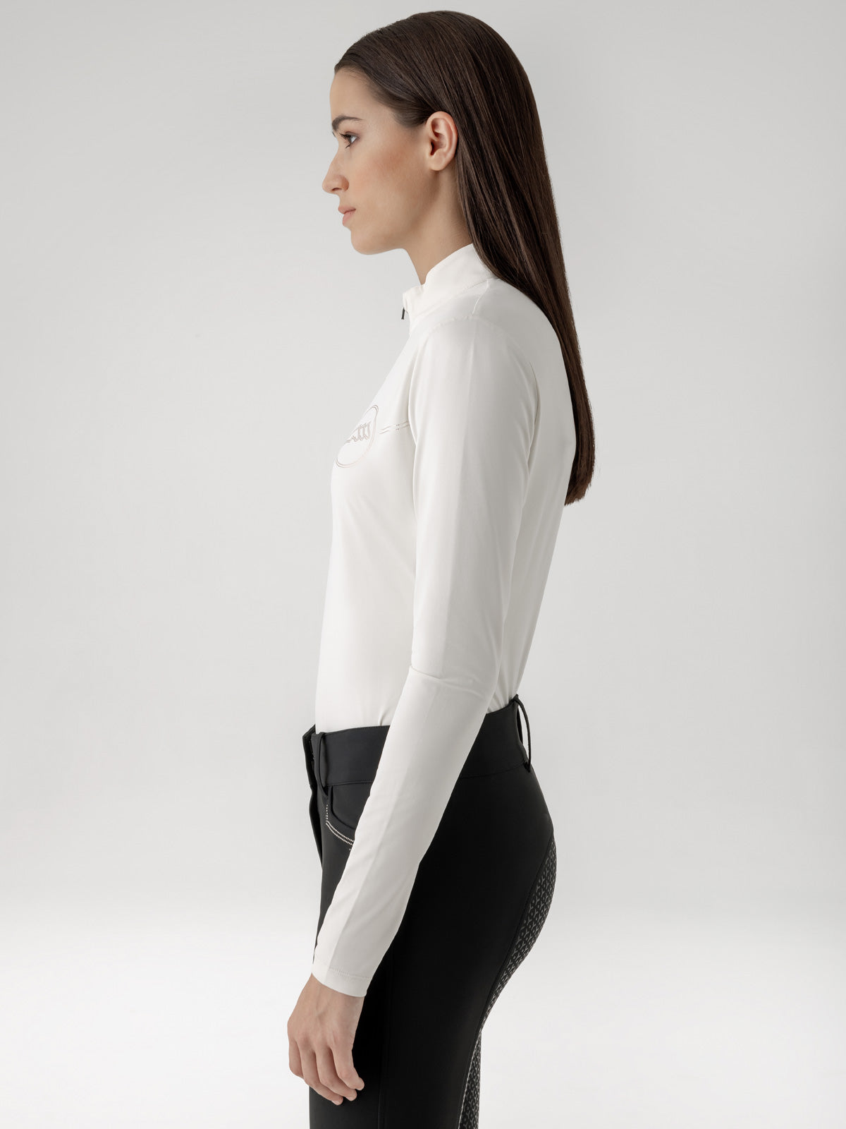Woman wearing a white long-sleeve shirt and black riding pants on a white background