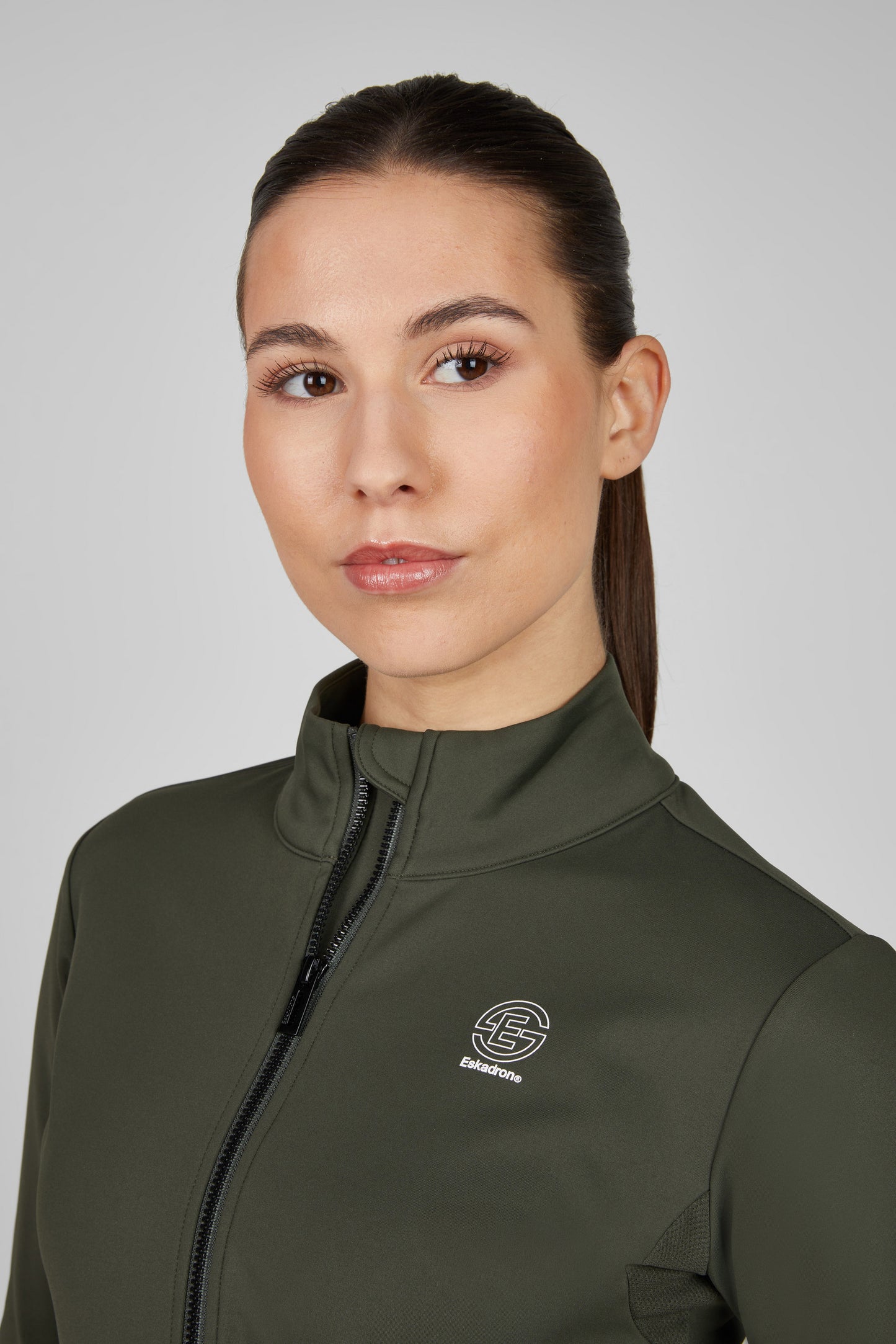 Woman wearing a green jacket with a logo on a gray background