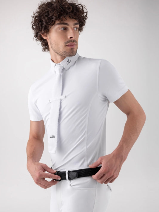 A man wearing a white short-sleeve polo shirt with a matching white tie and white trousers, adjusting a black belt against a light gray studio background.