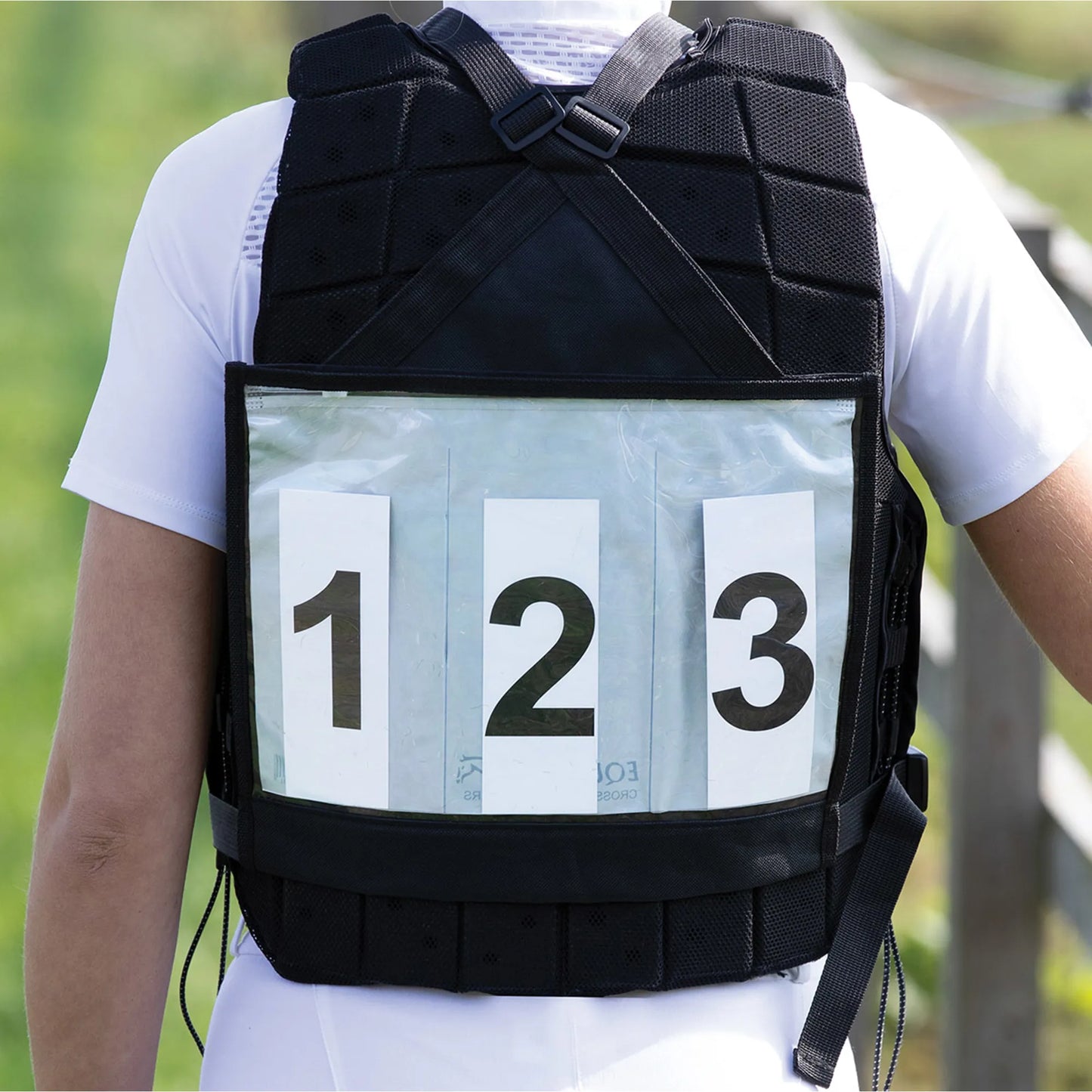 Person wearing a black backpack with numbered compartments outdoors.