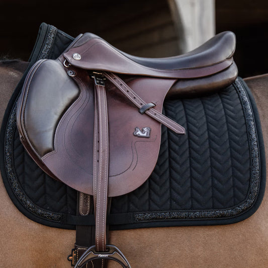 Brown leather saddle on a black quilted saddle pad with a blurred background