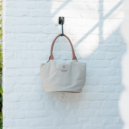 Beige tote bag with brown handle hanging on a white brick wall