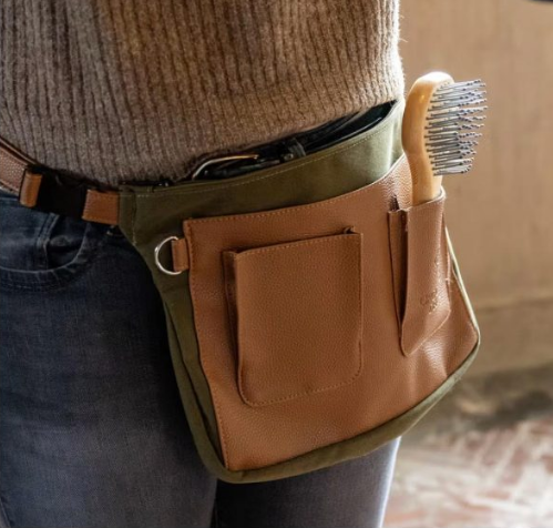 Person wearing a grooming deluxe plaiting bag including a brush, on a blurred background.