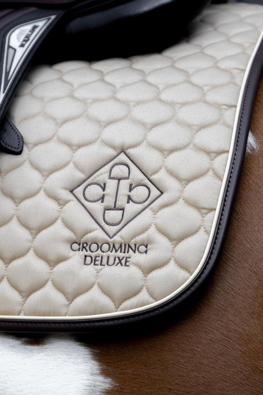 Close-up of a quilted saddle pad with 'Grooming Deluxe' branding on a horse's back.