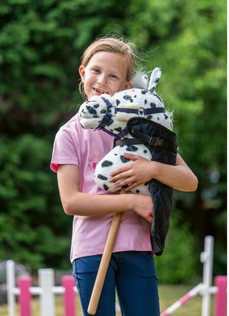 Girl holding a hobby horse wearing a navy rug with a blurred green background