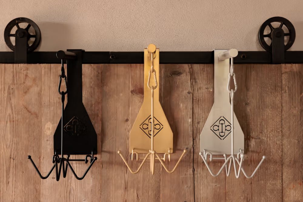 Three metal hooks with decorative designs on a wooden wall.