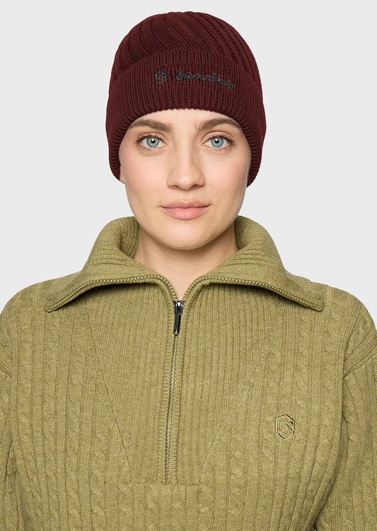A woman wearing a burgundy ribbed knit beanie with a small embroidered logo and an olive green ribbed quarter-zip pullover sweater, shown against a light gray studio background.