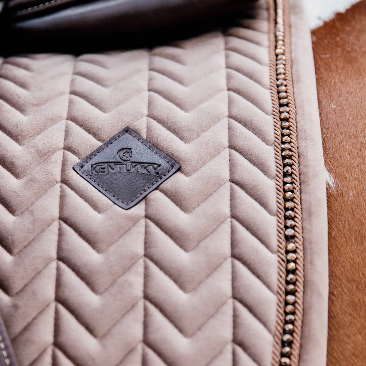 Quilted beige saddle pad with a 'Kentucky' brand patch on a brown leather background.