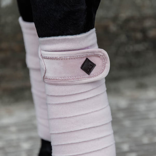 Close-up of pink protective leg wraps on a horse's legs with a blurred background.