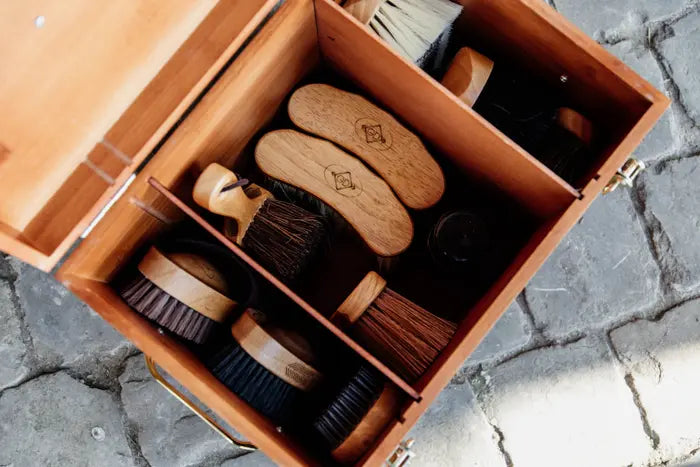 A deluxe stable grooming box made of bamboo, featuring multiple compartments and gold snap closure, with a cobblestone background.