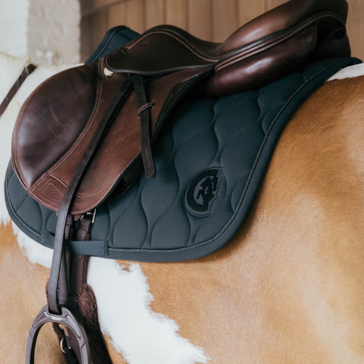Brown leather saddle on a horse with a visible brand logo.