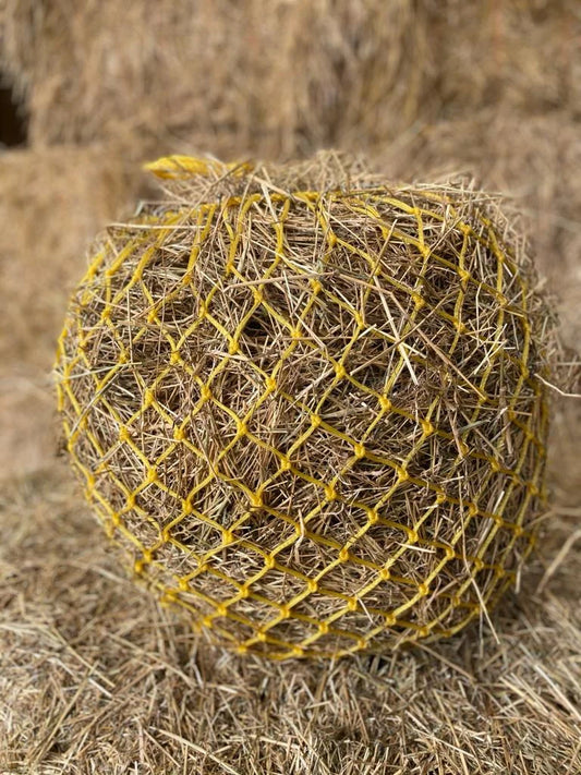 Hay bale wrapped in yellow netting on a field of hay.