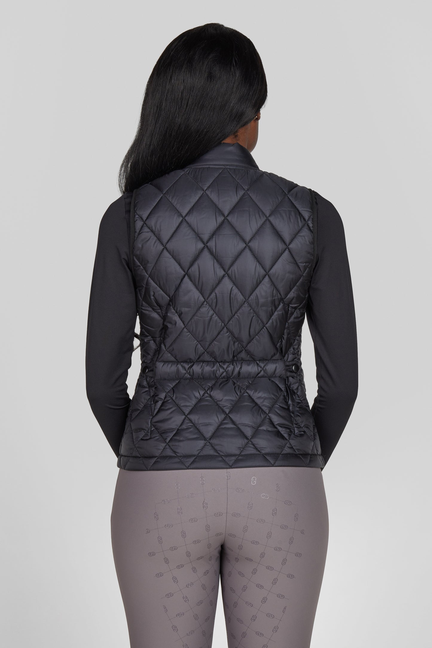 Person wearing a black quilted vest on a gray background