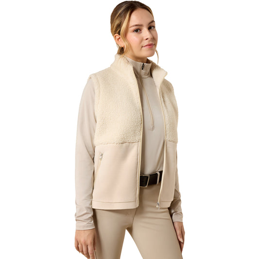 A woman modeling a beige fleece-lined zip-front vest over a matching beige long-sleeve top and beige pants, shown against a plain white studio background.