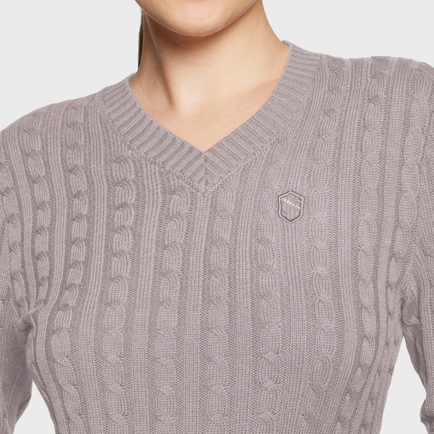 Close-up of a gray cable knit sweater with a brand logo on a light background