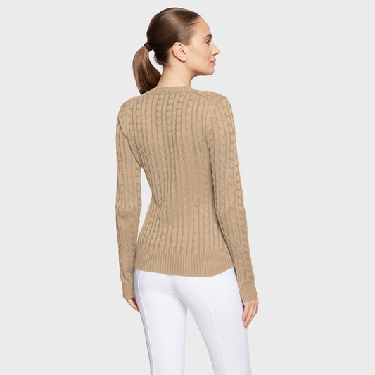 Woman wearing a beige ribbed sweater and white pants on a light gray background