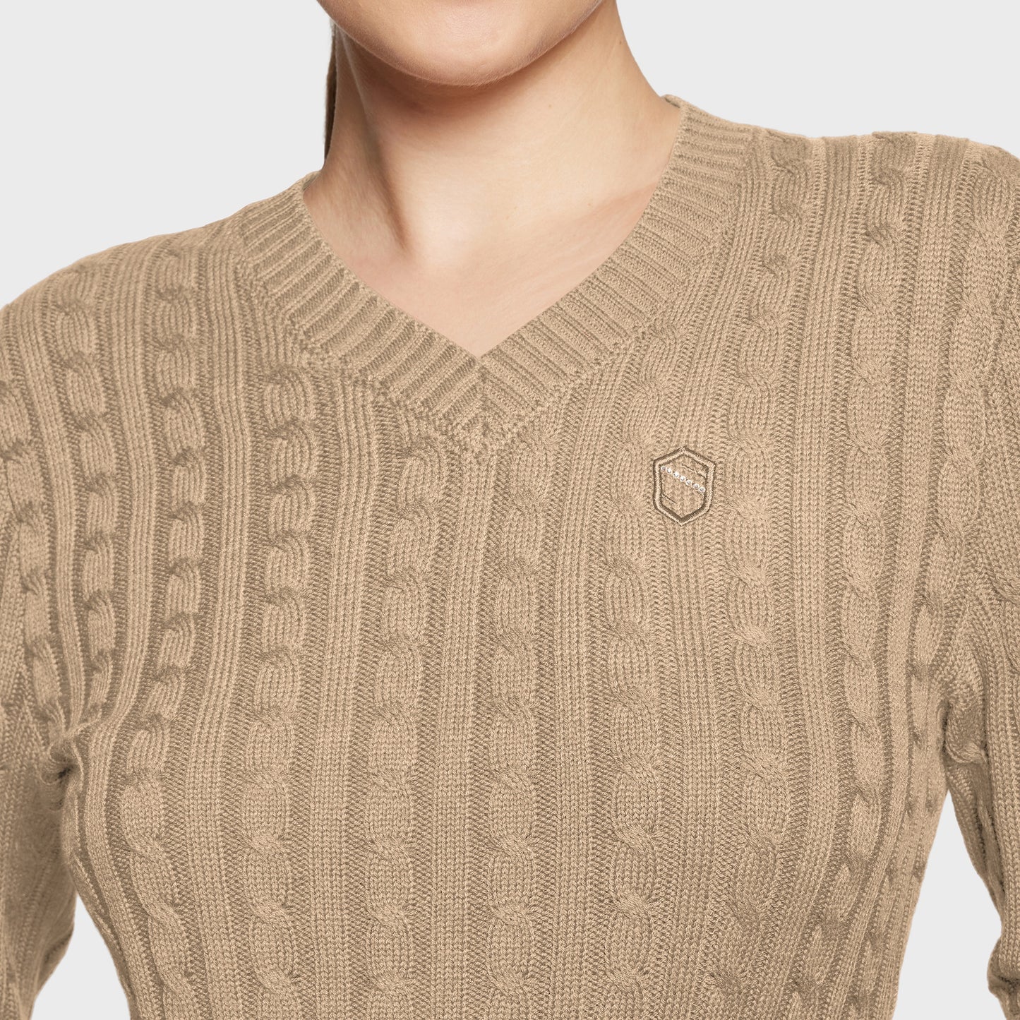 Beige cable knit sweater with a small logo on a light gray background