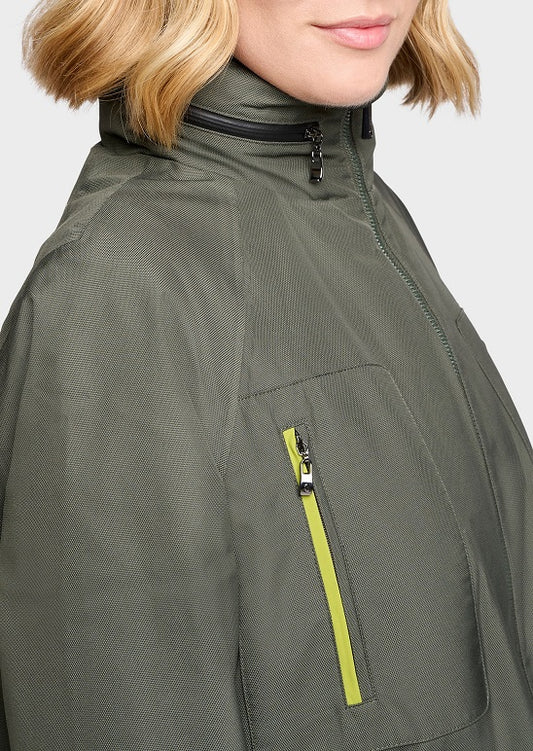 Close-up of a person wearing an olive green jacket with a high collar, black zipper trim, and a bright yellow-green accent zipper on the chest pocket.