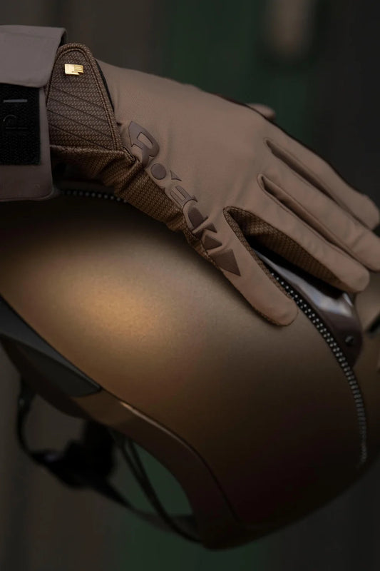 A close-up of a tan leather riding glove with a zipper and textured knit cuff, resting on a matching tan motorcycle helmet.