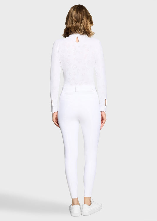 Woman wearing a white competition shirt and white breeches on a beige background