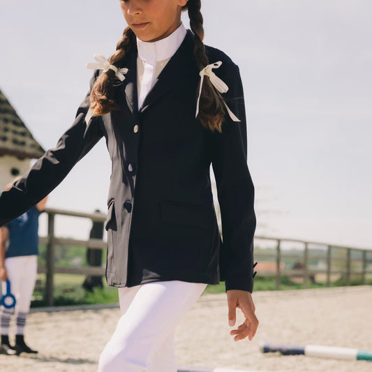Person wearing a black equestrian jacket with white accents outdoors.