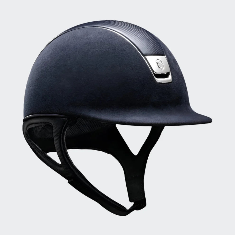 A dark navy blue equestrian riding helmet with a textured fabric finish, a black chin strap, and a small silver metal brand plate on the side, shown against a plain white background.