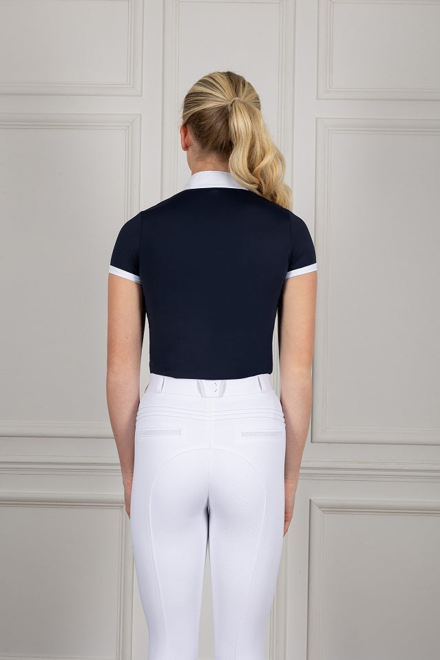 Person wearing equestrian attire including a navy top & white pants against a neutral background.
