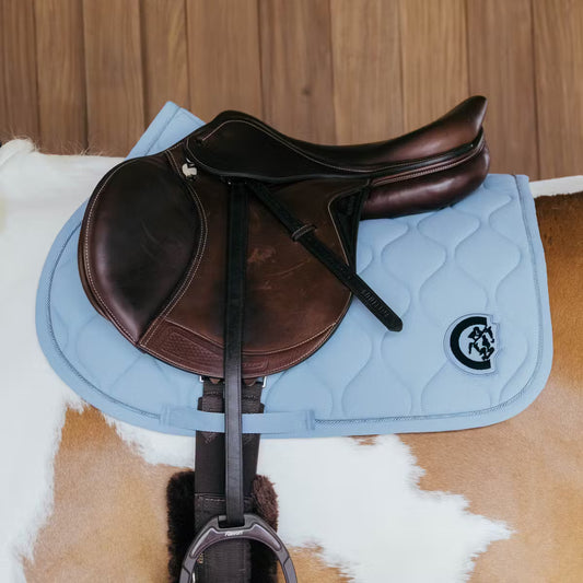 Brown leather saddle on a blue quilted saddle pad with a visible brand logo, placed on a horse.