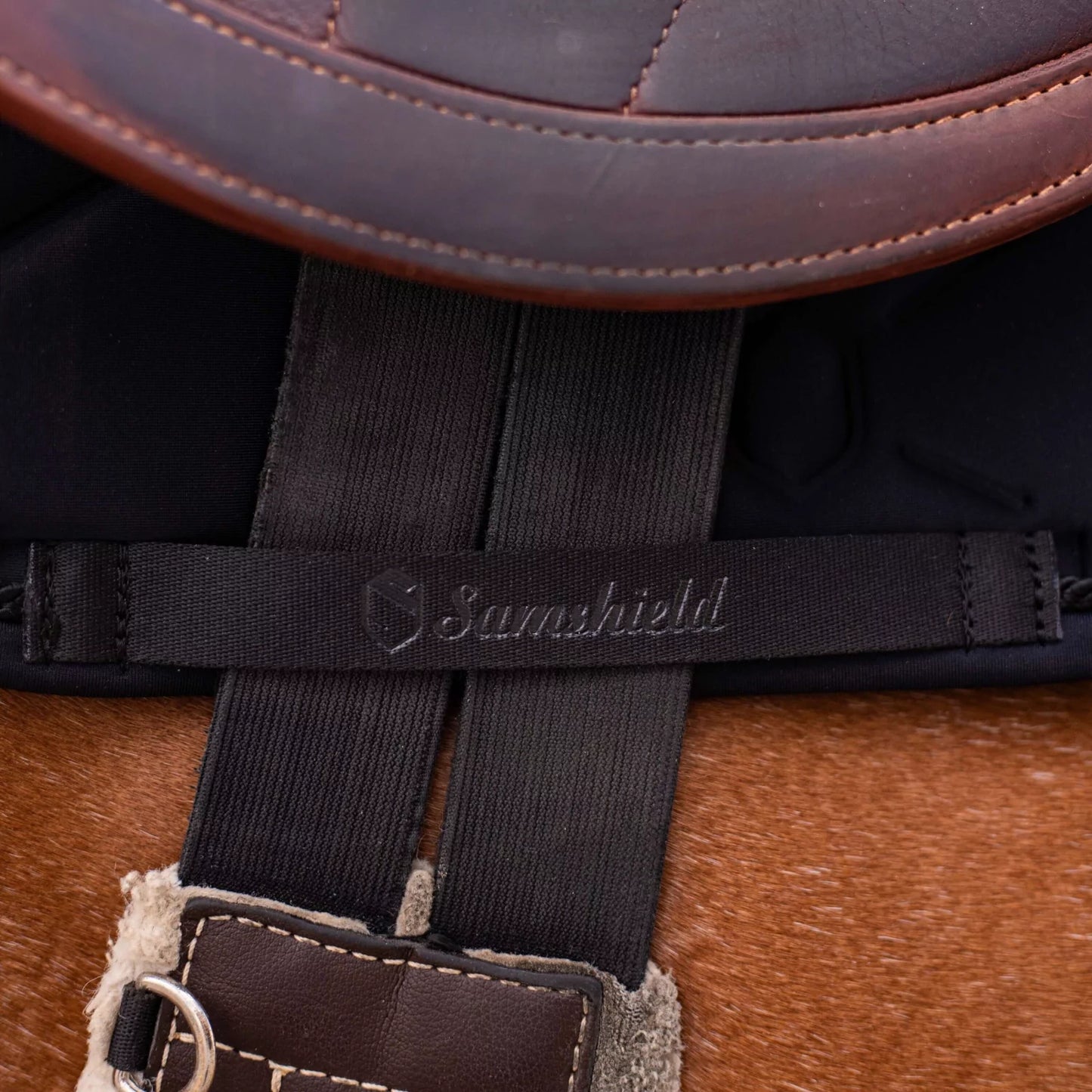 Detail of a girth fastening and a black saddle pad with Samshield logo