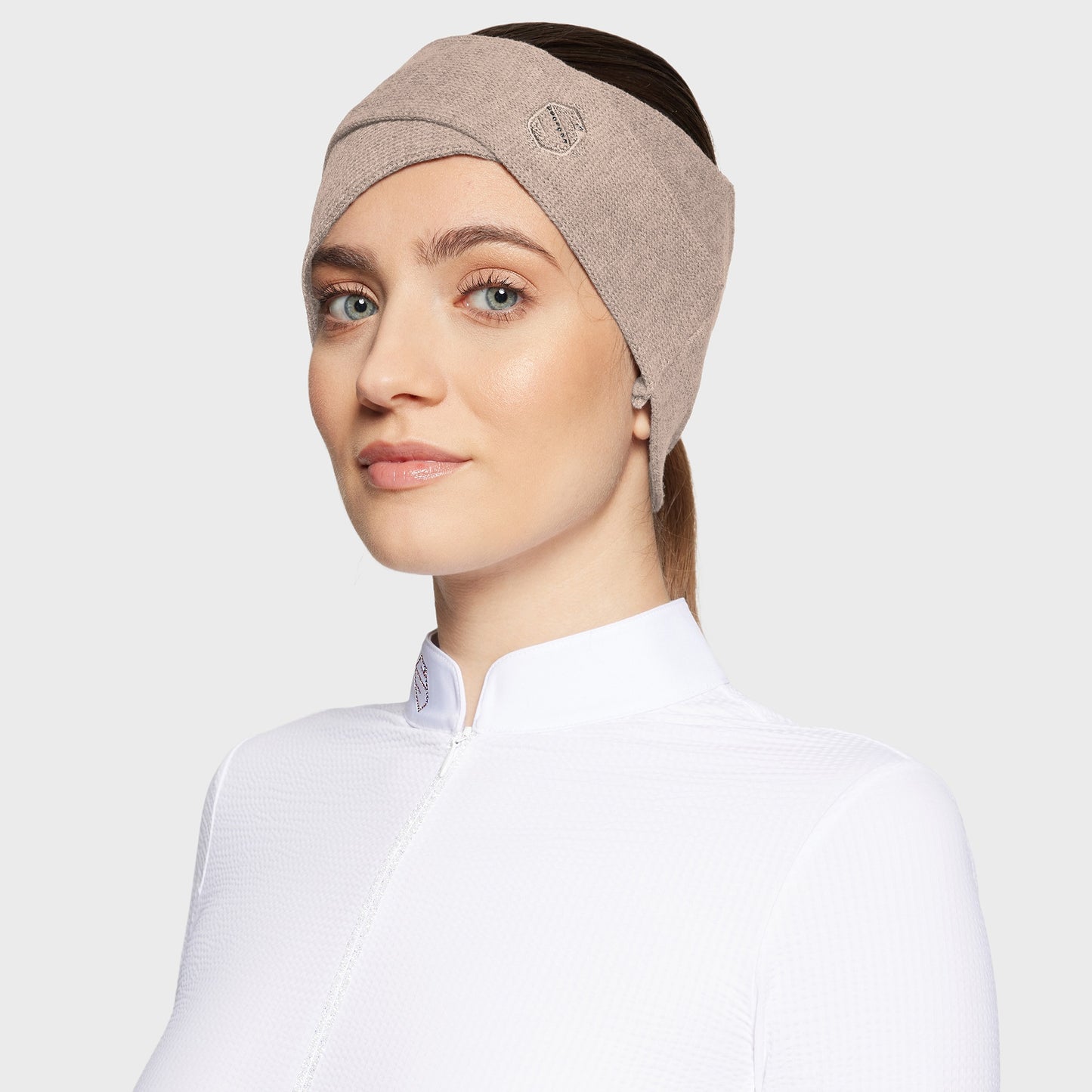 Woman wearing a beige criss cross headband with a white shirt on a white background