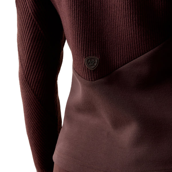 Close-up of a ribbed long-sleeve top in a deep burgundy or maroon color, showing a small shield-shaped logo patch on the chest and a smooth fabric panel across the lower torso.