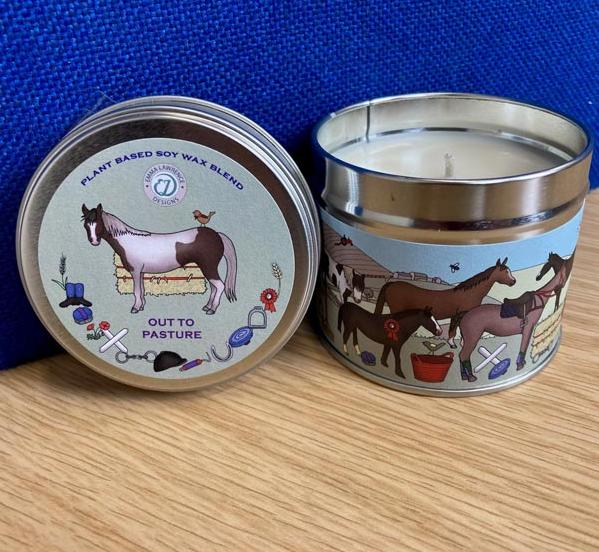 Candle in a tin with horse-themed design on a wooden surface and blue background