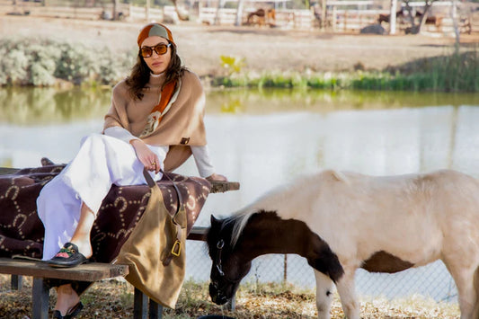 Lady sitting on a horse shoe brown blanke on a bench with a pony next to her and a lake behind her