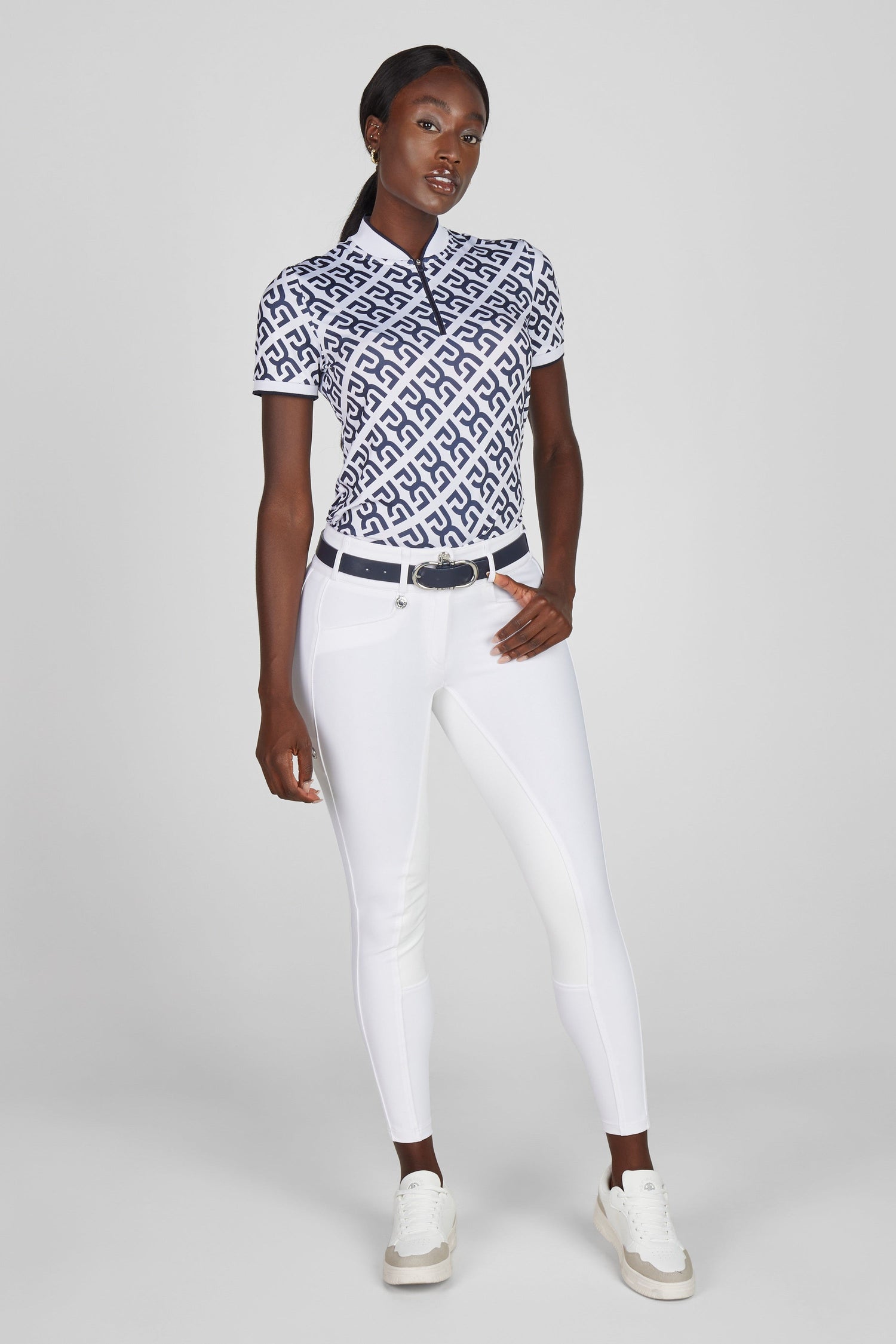 Model wearing a patterned white and blue top and a pair of white breeches and sneakers on a grey background