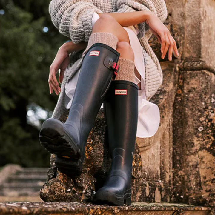 Woman wearing a pair of green hunter wellies, sitting on a stone wall.